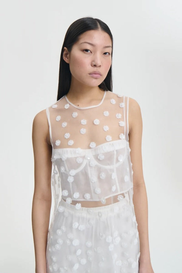 Alternate front view of white utania top on model wearing white brassiere and shorts, against a white background.