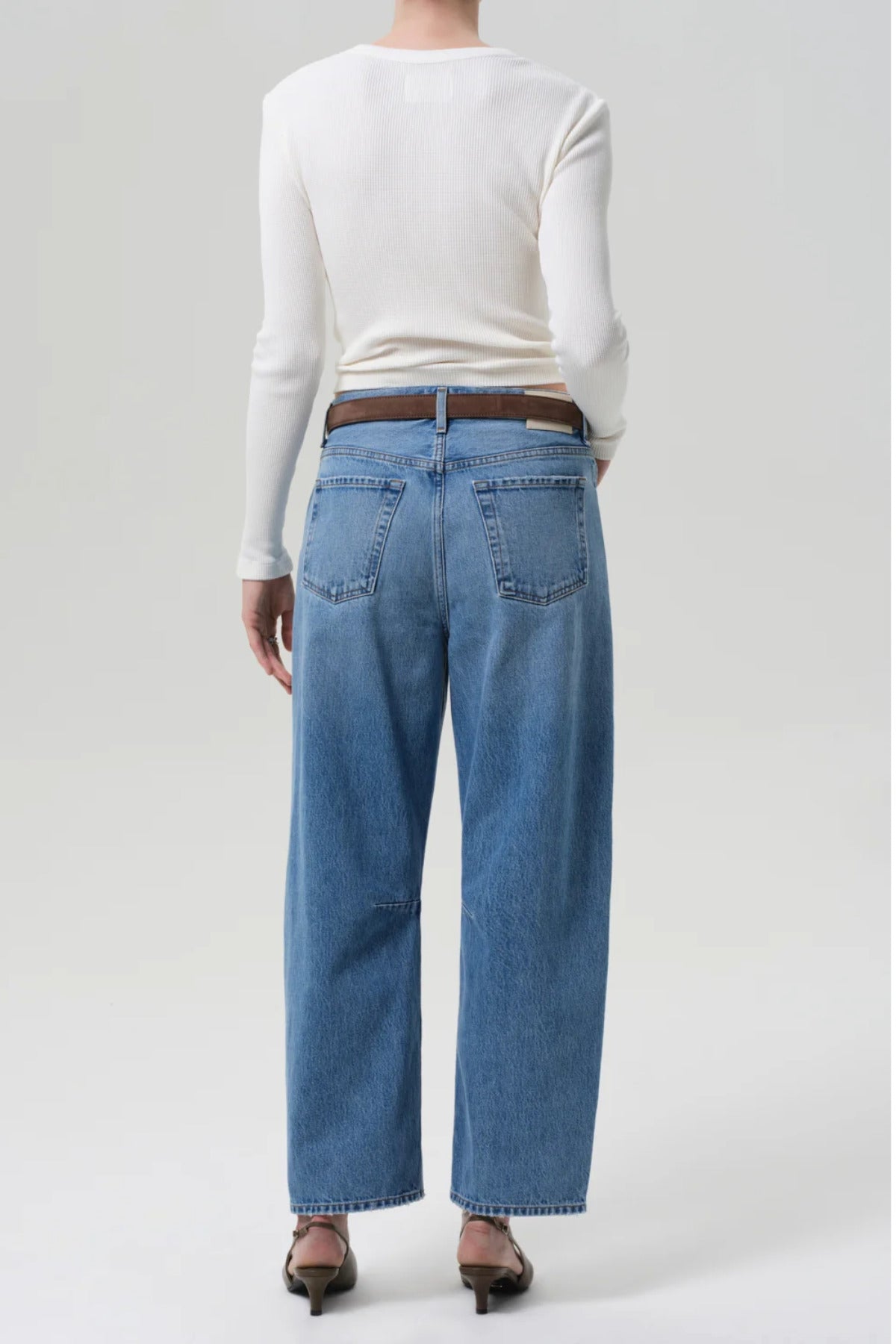 Back view of miro jean in corrin on model wearing a white t-shirt and brown heels, against a white background.