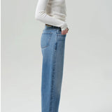 Side view of miro jean in corrin on model wearing a white t-shirt and brown heels. against a white background.