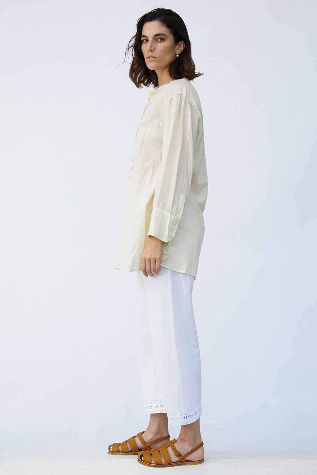 Side view of kora little subhash shirt on model wearing white pants and natural sandals, against a white background.