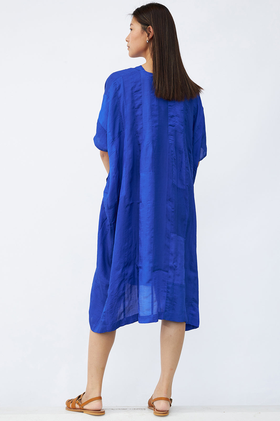 Back view of cobalt yoruba tunic on model wearing natural sandals against a white background.