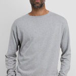 Front view of grey aries sweater on dark-haired model wearing black trousers, against a white background.