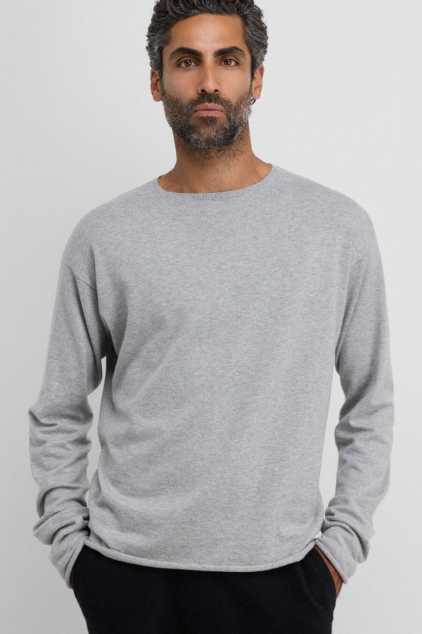 Front view of grey aries sweater on dark-haired model wearing black trousers, against a white background.
