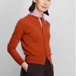 Front slanted view of dark orange no 300 little 2 cardigan on model wearing brown pants, against a white background.