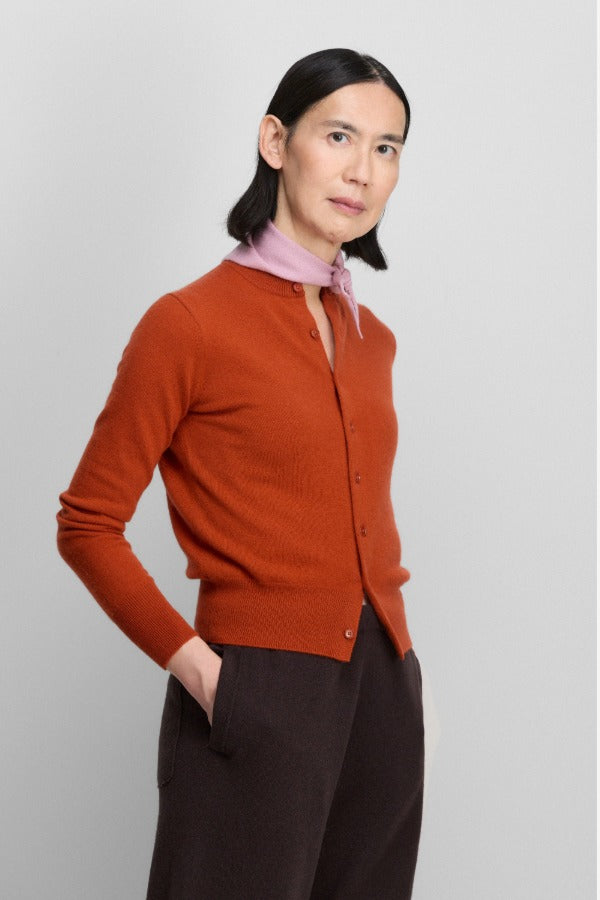 Front slanted view of dark orange no 300 little 2 cardigan on model wearing brown pants, against a white background.