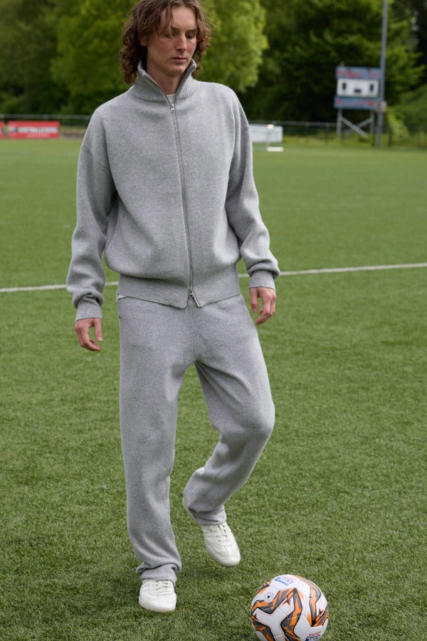 Front view of grey no 320 rush trouser on model wearing grey jacket and sneakers, against a grassy field background.