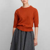 Front view of dark orange no 432 well lamb sweater on model wearing grey skirt, against a white background.