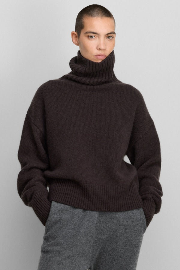Front view of dark brown no 434 crop xtra sweater on model wearing grey pants, against a white background.