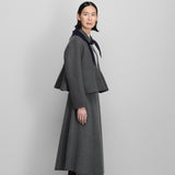 Side view of felt no 442 queen coat on model wearing grey skirt and heels, against a grey background.