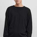 Front view of raven aries sweater on dark-haired model wearing black trousers, against  white background.