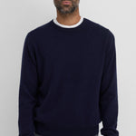 Front view of raven be classic sweater on dark-haired model wearing a white t-shirt underneath and grey trousers, against a white background.