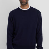 Front view of raven be classic sweater on dark-haired model wearing a white t-shirt underneath and grey trousers, against a white background.