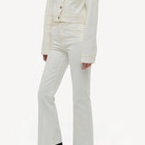 Side view of white ezra bootcut jean on model wearing white jean jacket and boots, against a white background.