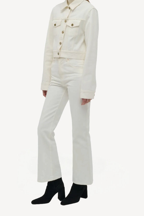 Side view of white ezra bootcut jean on model wearing white jean jacket and boots, against a white background.