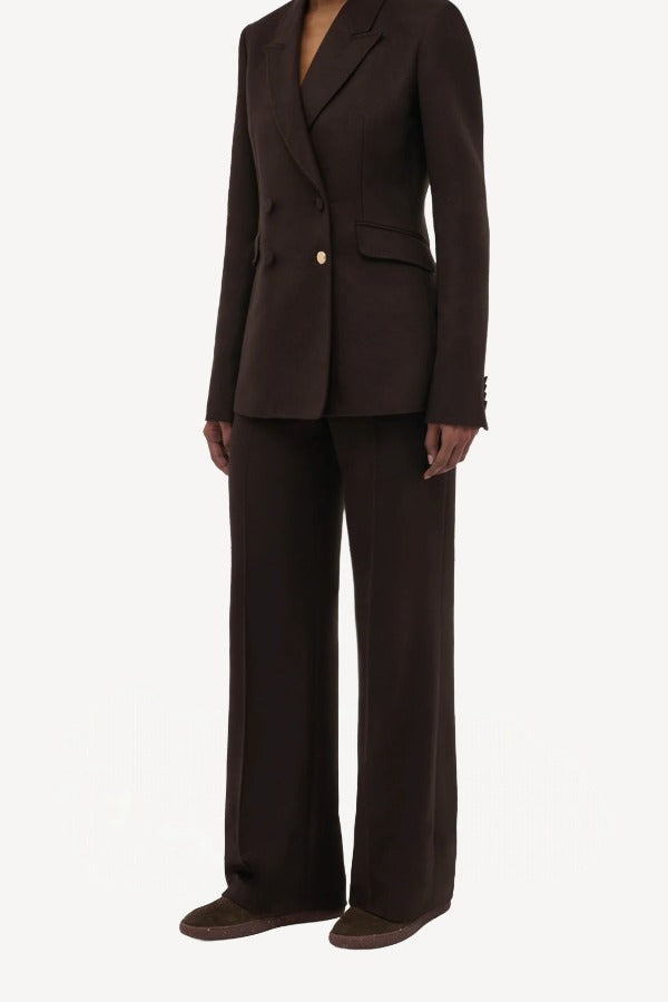 Side slanted view of chocolate vesta pant on model wearing stephanie blazer and sneakers, against a white background.