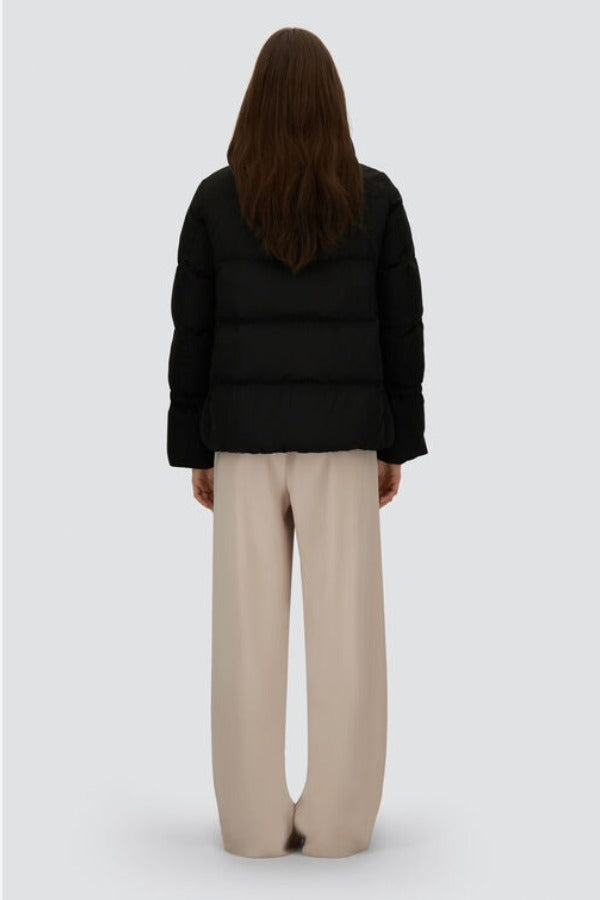 Back view of black jacket in arendelle on model wearing beige pants, against a white background.