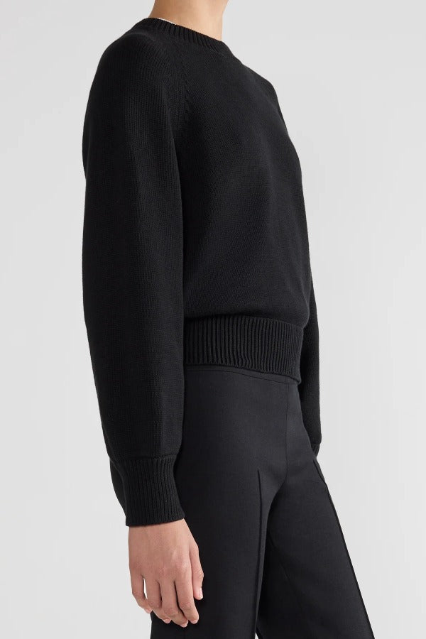 Side view of black lofty lara sweater on model wearing balck pants, against a white background.