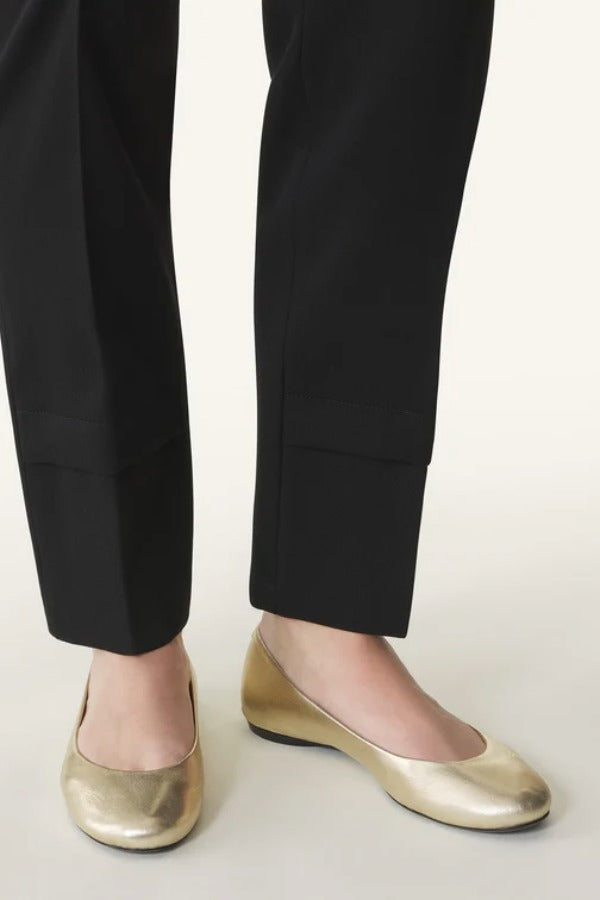 Front and side view of gold ballerina flats on model wearing black pants, against a white background.