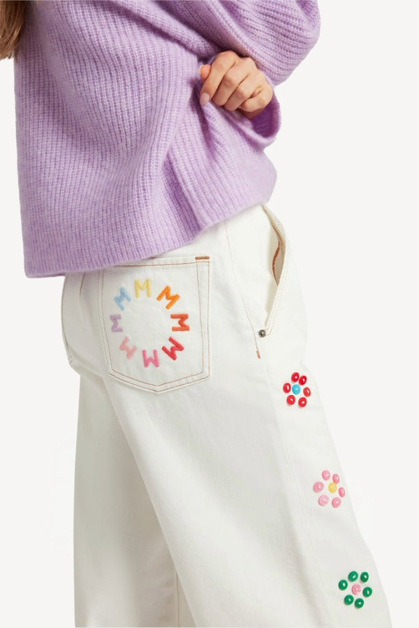 Side closeup view of lilac embroidered sweater on model wearing white denim, against a white background.