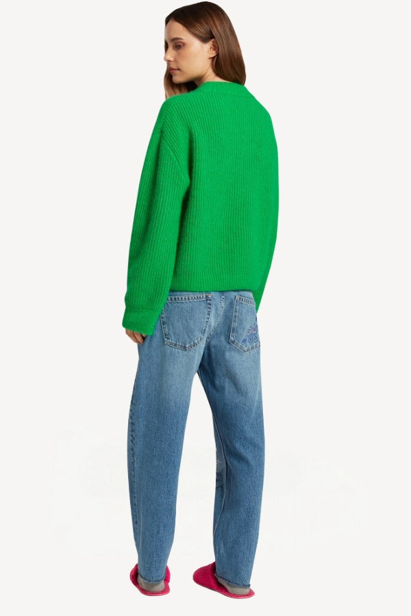 Back view of denim embroidered scribble jean on model wearing green sweater and pink slides, against a white background.