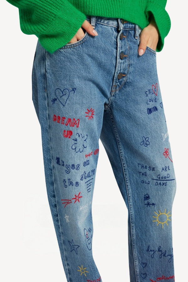 Front closeup view of denim embroidered scribble jean on model wearing green sweater, against white background