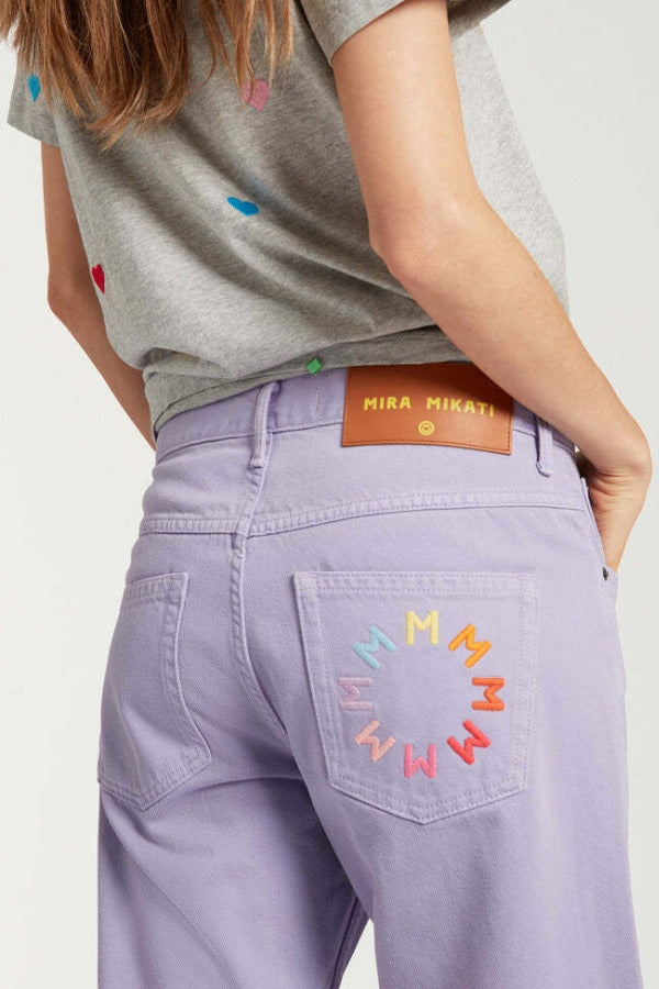 Back closeup view of lilac garment dyed jeans on model wearing grey shirt with hearts, against a white background.