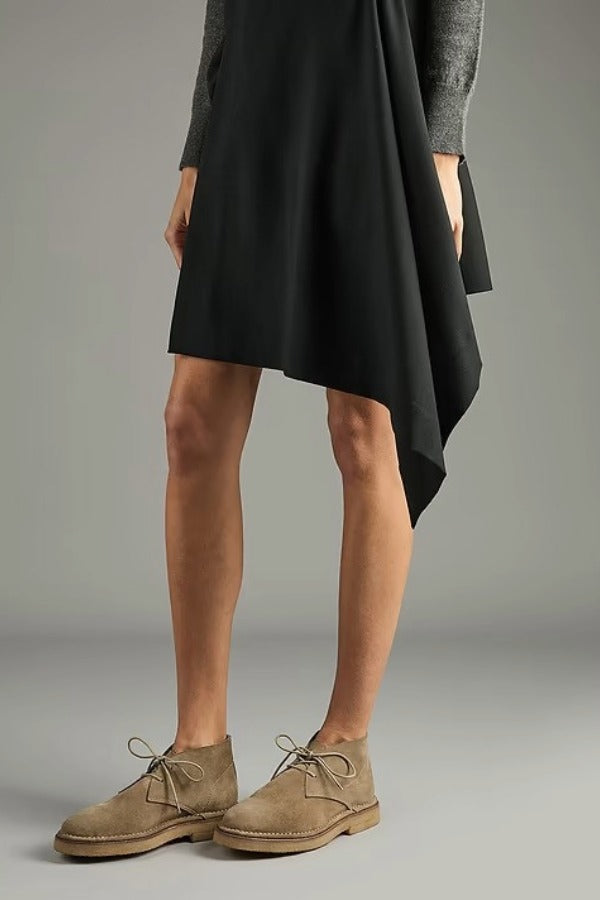 Side view of pair of sand antoine desert boots on model wearing black dress, against a white background,