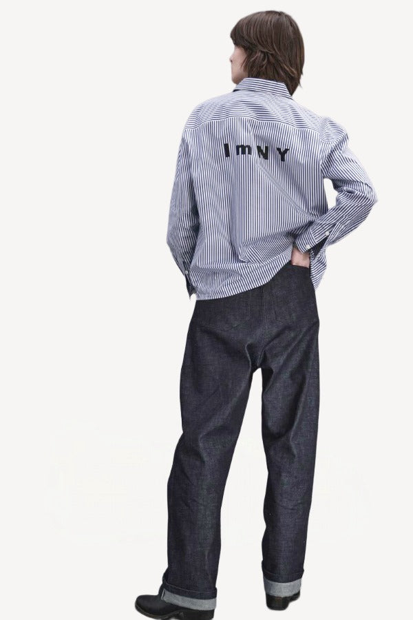 Back view of denim M Pants on model wearing stripe shirt and boots, against a white background