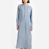 Front view of dusty blue tunic dress on dark-haired model wearing small white wedge heels, against a white background.