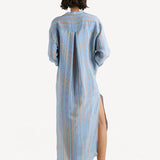 Back view of dusty blue tunic dress on model wearing short white wedge heels, against a white background.