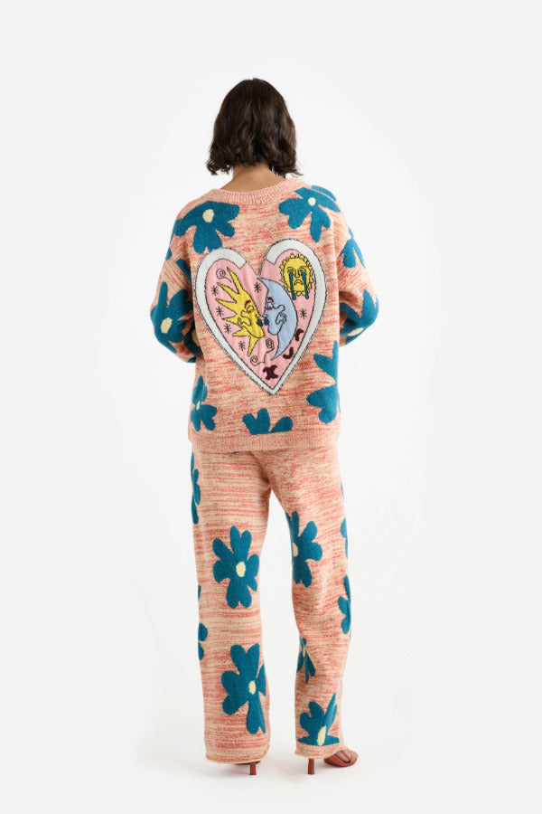 Back view of multi floral the elder statesman sun and moon cardigan on model wearing matching pants and heels, against white background.