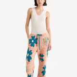 Front view of multi floral drawstring pants on model wearing white tank top and sandals, against a white background.