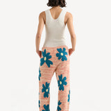 Back view of multi floral drawstring pants on model wearing white tank top and sandals, against a white background.