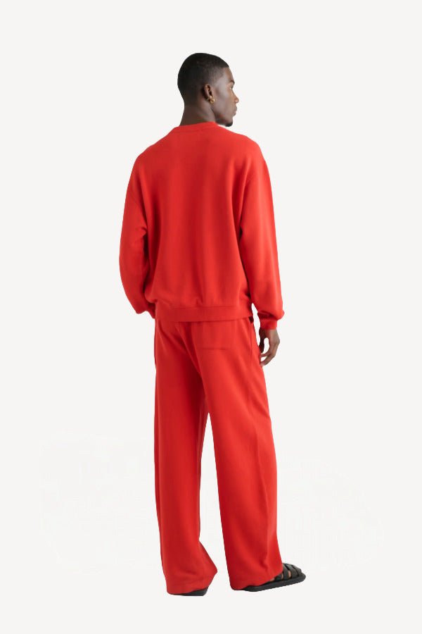 Back view of sanguinello daly crew top on dark-haired model wearing red trousers, against white background.