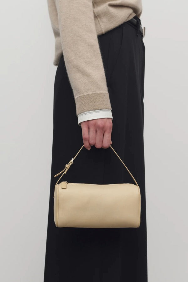 Front view of sand 90's bag on model wearing a beige sweater and black pants, against a white background.