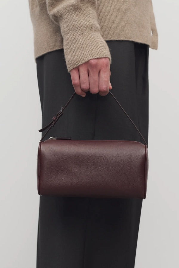 Front view of burgundy 90's bag on model wearing grey pants and ecru sweater, against a white background.