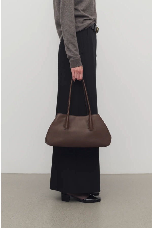 Front view of deep brown alger shoulder bag on model wearing black pants and brown melange sweater, against a white background.