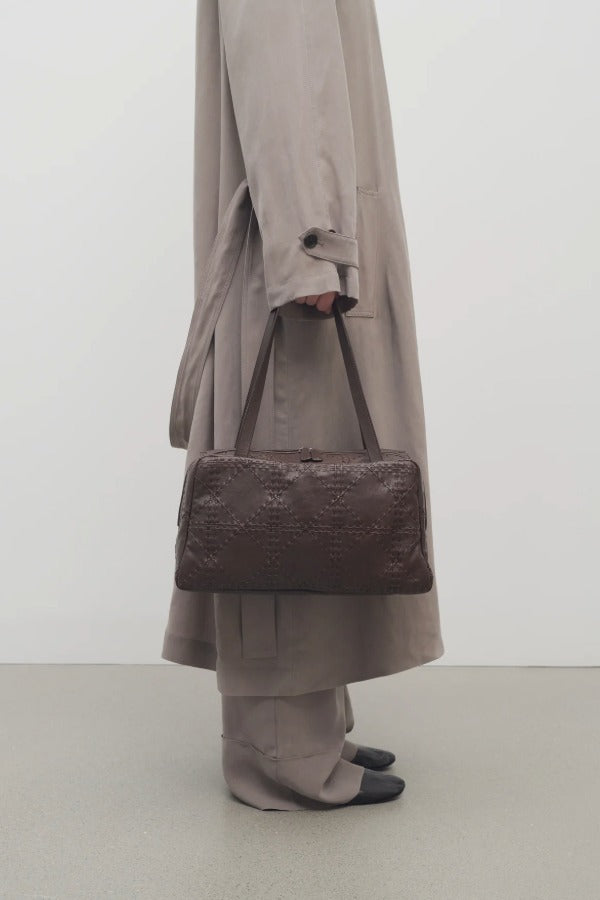 Front view of brown astra bowling bag on model wearing taupe trench coat pants an ballet flats, against a white background.