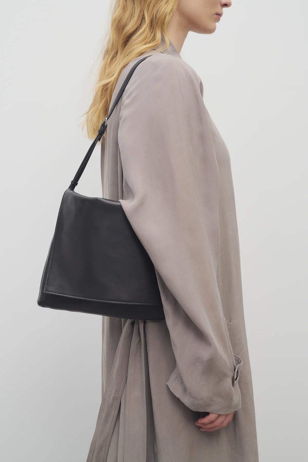 Front view of black leather bag on white background, with model wearing khaki coat.