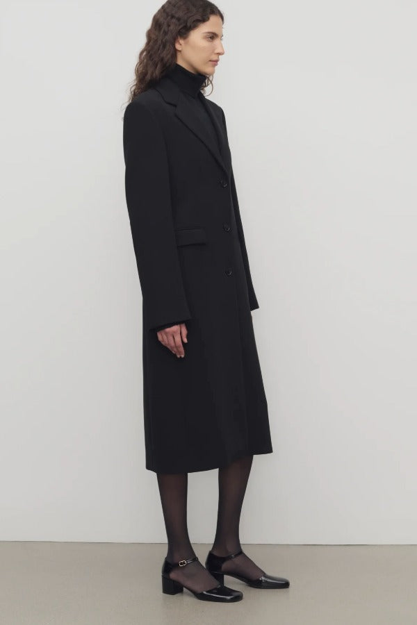 Side view of black cerys coat on model wearing black heels, against a white background.
