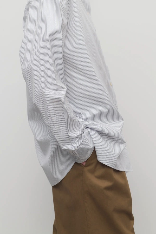 Side view of blue/white cotton sisilia shirt on model wearing camel trousers, against a white background.