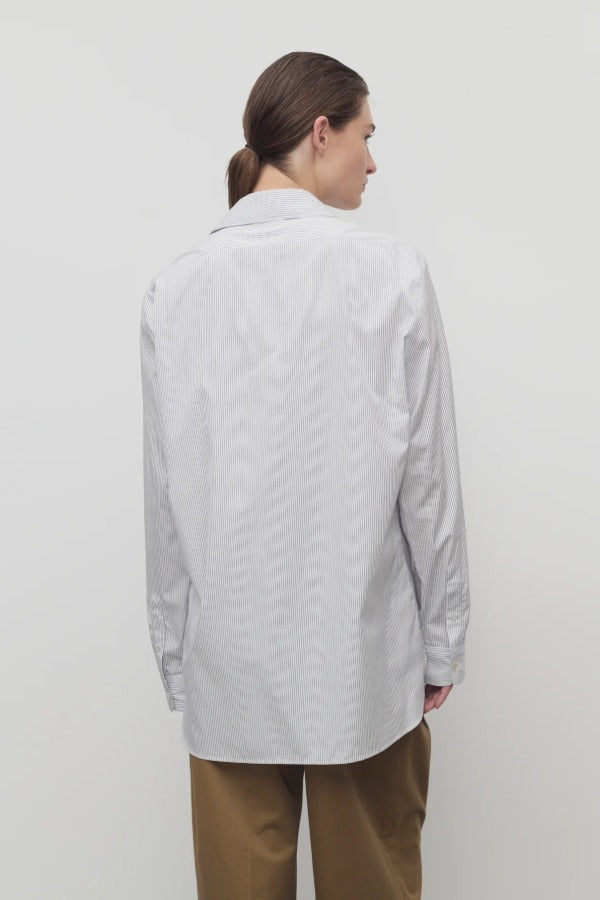 Back view of blue/white sisilia shirt on model wearing camel trousers, against a white backgorund,