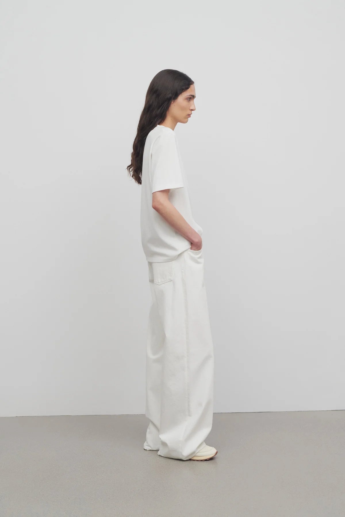 Side view of white eglitta jean on model wearing white t-shirt and sneakers, against a white background.