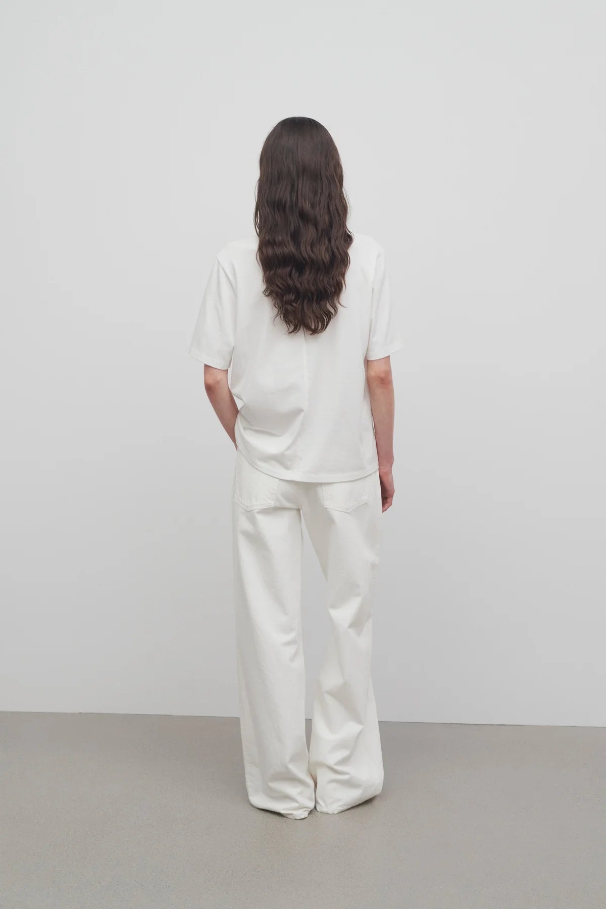 Back view of white eglitta jean on model wearing white t-shirt, against a white background.