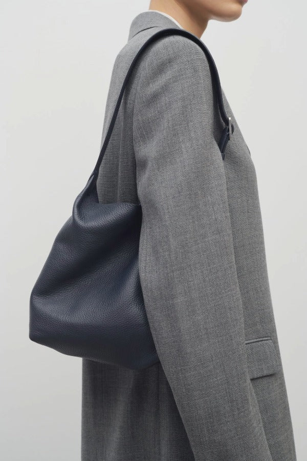 Front view of blu notte isa shoulder bag on model wearing grey coat, against a white background.
