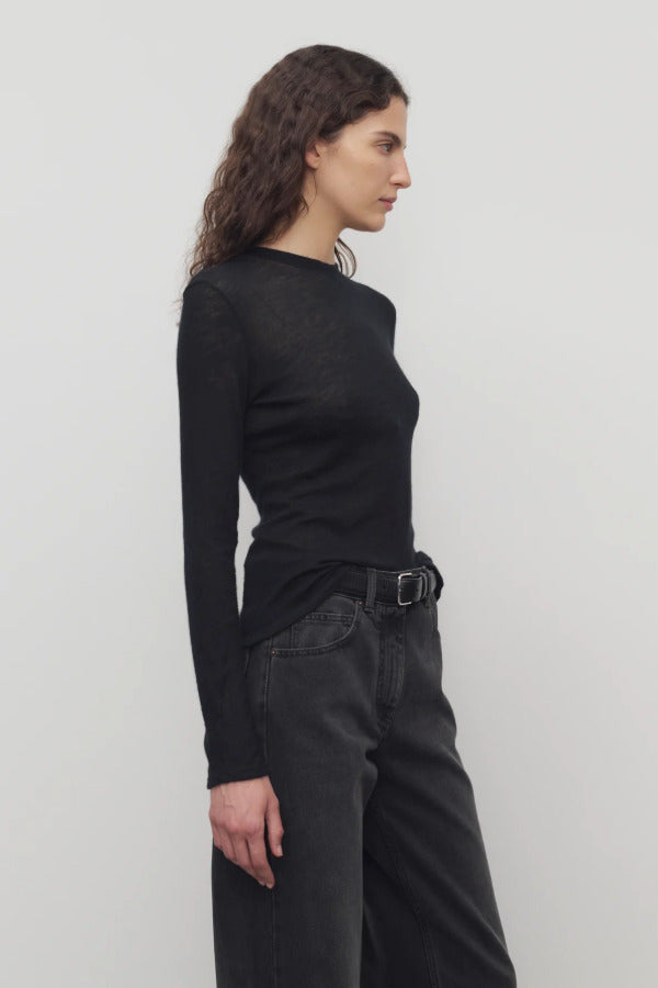 Side view of black iverness top on model wearing black jeans and belt, against a white background.