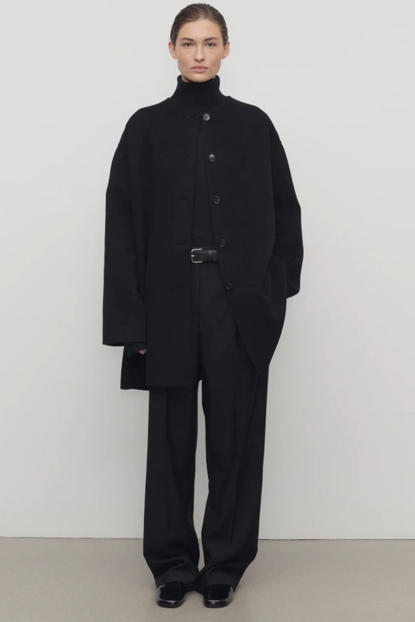 Front view of black kala coat on model wearing black turtleneck and trousers, against a white background.