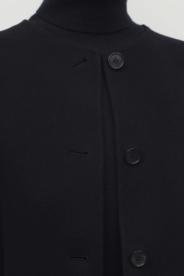 Front closeup view of black kala coat on model wearing black turtleneck, against a white background,