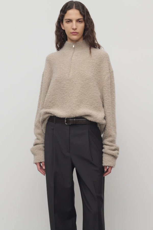 Front view of beige lethara sweater on model wearing black pants and a brown belt, against a white background.