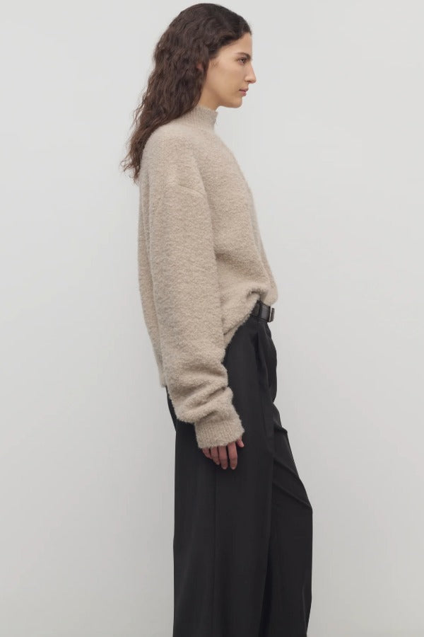 Side view of beige lethara sweater on model wearing black pants, against a white background.